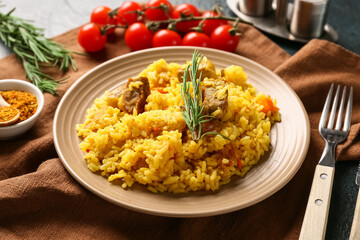 Plate of tasty pilaf with rosemary, cherry tomatoes and bowl of spices on dark background, closeup