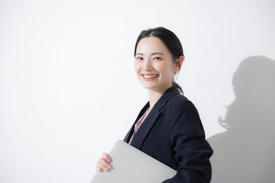 パソコン持ってスーツを着た立つ若いかわいい女性のビジネス上半身　かわいい白背景の営業などリクルートのイメージ カメラ目線