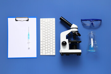 Modern microscope with keyboard, flask, clipboard and safety glasses on blue background