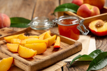 Cutting board with sweet peaches and jar of jam on wooden table