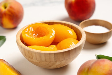Wooden bowl of tasty canned peaches and sugar on light background