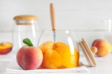 Glass jar of tasty canned peaches and fresh fruits on light wooden table