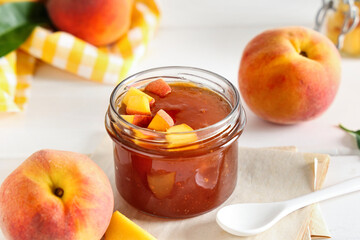 Glass jar of tasty peach jam and fresh fruits on light wooden table
