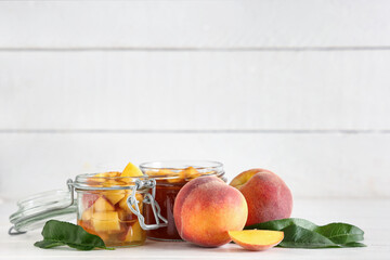 Jars of tasty peach jam and fresh fruits on light wooden table