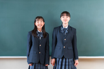 教室の黒板の前に立つ制服姿の友達,小学生,中学生,高校生の女子生徒
