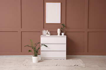 Chest of drawers and houseplant near brown wall in interior of living room