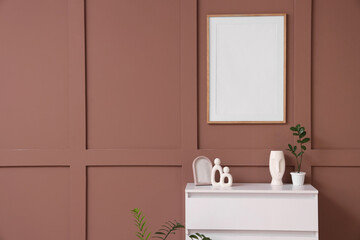 Chest of drawers with houseplant, vase and statuette near brown wall in living room, closeup