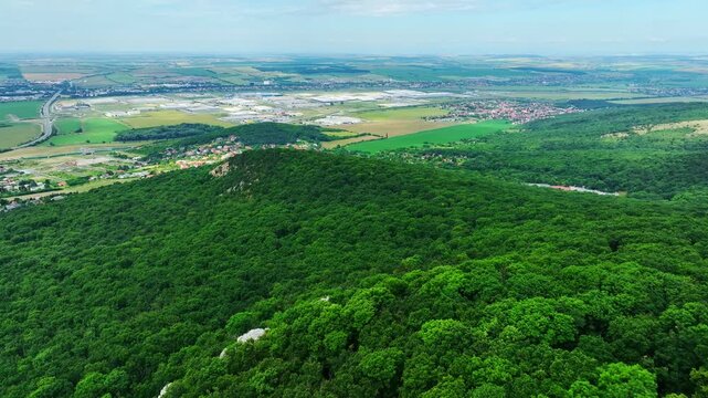 Beautiful drone shot from Zobor hill capturing the panoramic view of Nitra city, forested hills, and surrounding farmland in Slovakia.