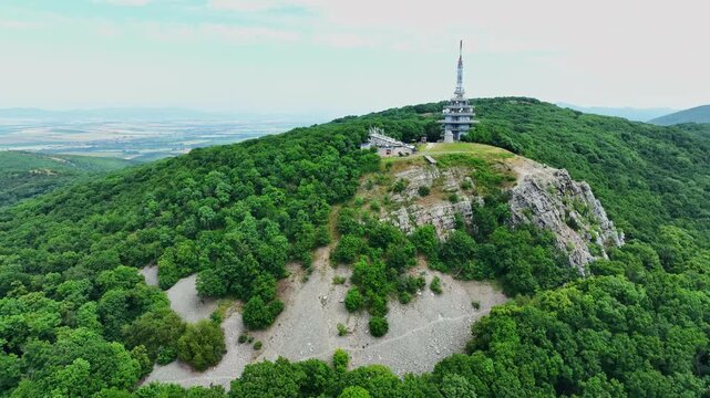 Drone footage of Zobor hill in Nitra, Slovakia, featuring lush forest, rocky slopes, and a tall broadcasting tower on the summit.
