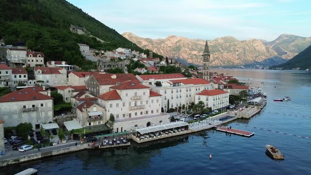 Perast town on bay of Kotor, romantic waterfront restaurant patios in evening, Saint Nicholas catholic church bell tower, Aerial, establishing shot