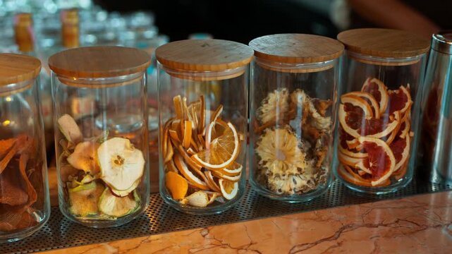 Glass jars filled with dried apple orange pineapple and citrus slices displayed at tropical beach cocktail bar - slow motion parallax
