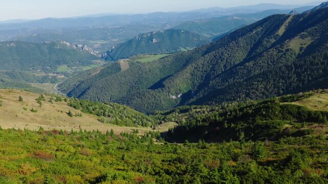 Scenic drone shot from Chleb peak in Mal&aacute; Fatra, Slovakia, overlooking a lush green valley with forested slopes, meadows, and a rustic mountain shelter.