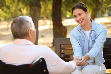 Obraz premium Senior woman in wheelchair with caregiver holding hands outdoors