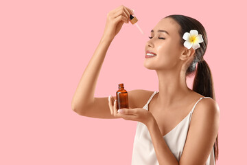 Fototapeta premium Young woman applying serum with vitamin E on pink background