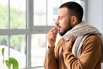 Ill young man taking throat lozenge at home