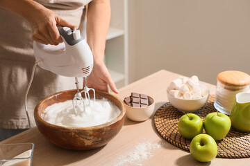 Woman whipping egg albumen with mixer in kitchen, closeup