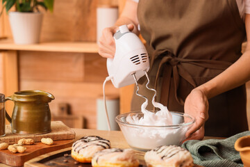 Woman whipping egg albumen with mixer in kitchen, closeup