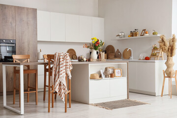 Interior of light kitchen with table, counters and autumn flowers in vase