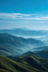 Misty mountain range landscape.  A hazy, panoramic view of rolling hills and mountains.  Soft, pastel blue-green hues.  Clear, light blue sky.  Suggests a tranquil, remote location