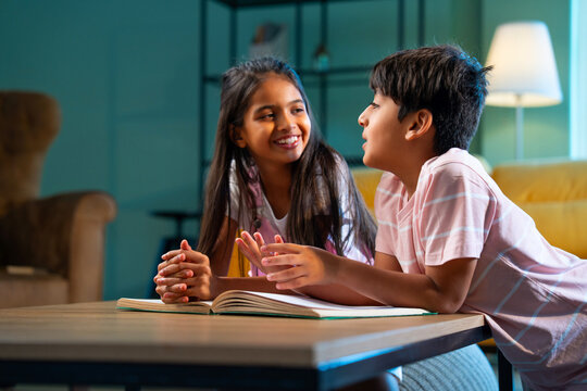 Indian Asian siblings kids reading book and studying together at home in a modern family lifestyle