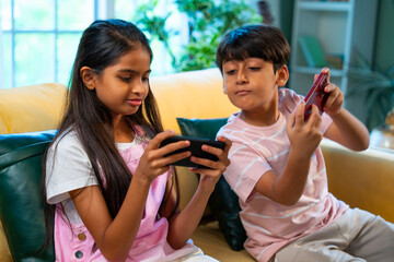 Indian Asian siblings kids using smartphones for mobile games while enjoying fun at home together