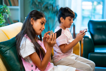 Indian Asian siblings kids using smartphones for mobile games while enjoying fun at home together