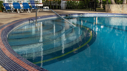 Swimming pool at the resort. The blue tiled bottom, the steps are visible through the clear water. Metal handrails. A row of deck chairs nearby. Cuba. Varadero. Hotel.