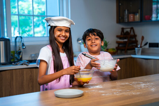 Indian sibling kids cook with eggs and flour in modern kitchen, playful childhood moment