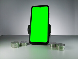 Picture of a phone showing green screen and stack of coins in sides. This photo can be used for Economy or money related advertisement