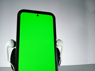 Picture of a smartphone showing green screen with earphones attached. This photo is taken with white background. This photo can be used for musical theme advertisement or music related promotion