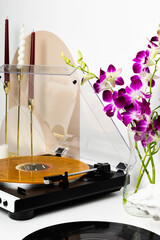 A vinyl record player with a transparent dust cover and a marbled orange record is the main focus of this minimalist setup. Surrounded by decorative candles and wooden accents, it creates a stylish an
