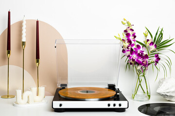 A vinyl record player with a transparent dust cover and a marbled orange record is the main focus of this minimalist setup. Surrounded by decorative candles and wooden accents, it creates a stylish an