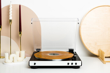 A vinyl record player with a transparent dust cover and a marbled orange record is the main focus of this minimalist setup. Surrounded by decorative candles and wooden accents, it creates a stylish an