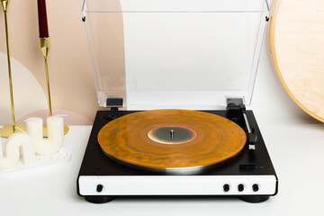 A vinyl record player with a transparent dust cover and a marbled orange record is the main focus of this minimalist setup. Surrounded by decorative candles and wooden accents, it creates a stylish an