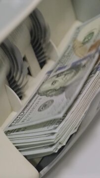 Stacks of US dollars being processed and counted in an automatic money counting machine.