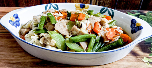 A favorite dish is capcay vegetables mixed with meatballs served in a bowl. A brown background.
