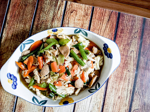 A favorite dish is capcay vegetables mixed with meatballs served in a bowl. A brown background.
