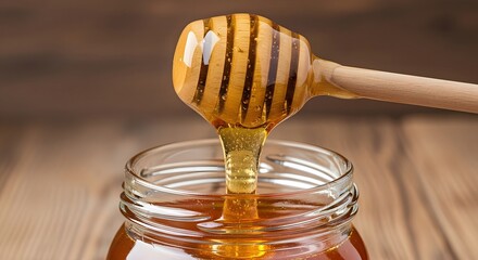 Golden honey dripping from wooden dipper into glass jar close-up sweet natural food