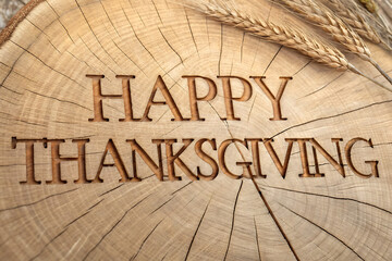 Rustic happy thanksgiving message carved into a wooden slice with wheat stalks in the background