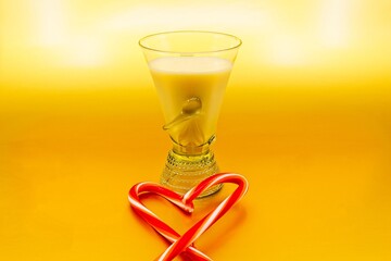 Fancy glass of eggnog . There are peppermint sticks forming a heart in the foreground. The background is metallic gold.