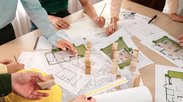 Architect and safety engineer discussion about building construction use blueprint on table with architectural document, measurement tool and wooden block scatter around at modern office. Delineation.