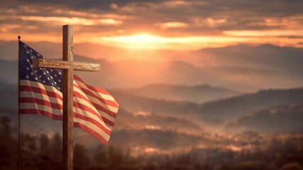 A stunning sunset casts warm colors over a serene mountain view. An American flag waves gently in the breeze next to a wooden cross