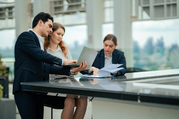 Professionals gathered outdoors, sharing ideas and reviewing data on laptop, representing teamwork, creative collaboration, and dynamic corporate culture. Business group doing work on rooftop hotel.