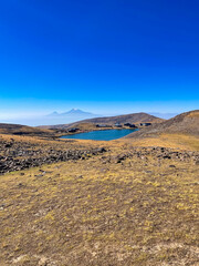 The majestic Aragats mountain range, towering over the vastness of Armenia. Rugged rocky peaks blend in with clear blue skies, creating an atmosphere of freedom and grandeur. The gaze goes into the