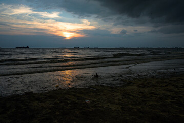 Sunset Over a Quiet Beach With Ships on the Horizon and Dark Clouds