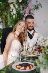 The bride and groom at the newlyweds' table, decorated with many flowers. 