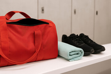 Red gym bag, black sneakers, and mint towel on white bench in modern locker room, fitness preparation essentials