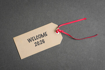 Welcome 2026 on paper tag with red ribbon, on top of dark gray surface.