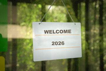 Signboard, Welcome 2026, behind glass door of a business store.