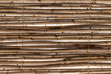 Close-up rustic texture of a handmade wooden fence created from natural branches and twigs tied with rope. Authentic organic background representing eco-friendly design, natural materials